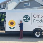 White EZ Office Products delivery van with a sunflower logo, parked on a residential street with a person pointing at it.