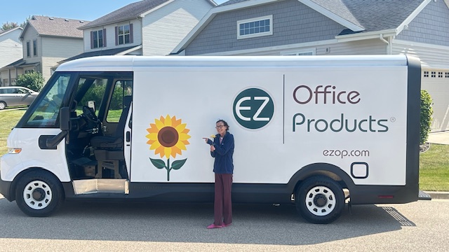 White EZ Office Products delivery van with a sunflower logo, parked on a residential street with a person pointing at it.
